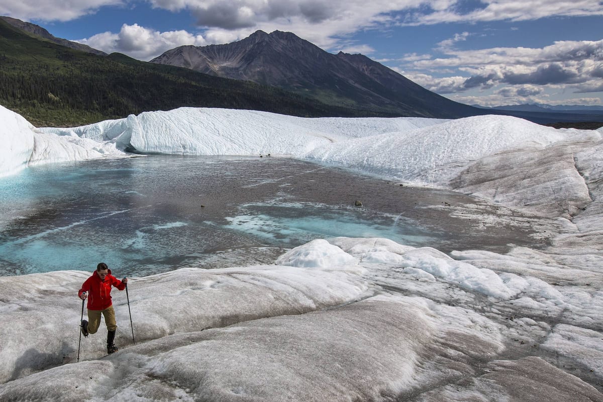 A hiker in a red jacket crossing the Root Glacier in Wrangell-St. Elias National Park, Alaska.