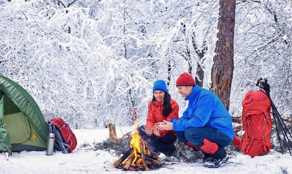 A couple enjoying a campfire at the forest during winter