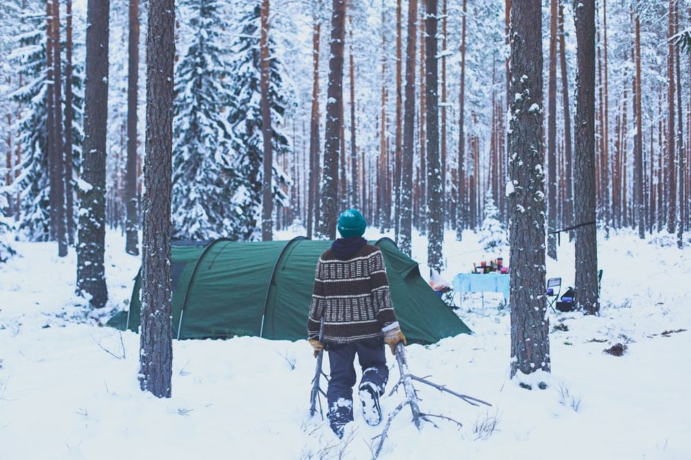 a man towards his tent while carrying twigs during winter camping
