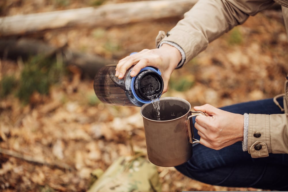 Person pouring water into a mug while camping