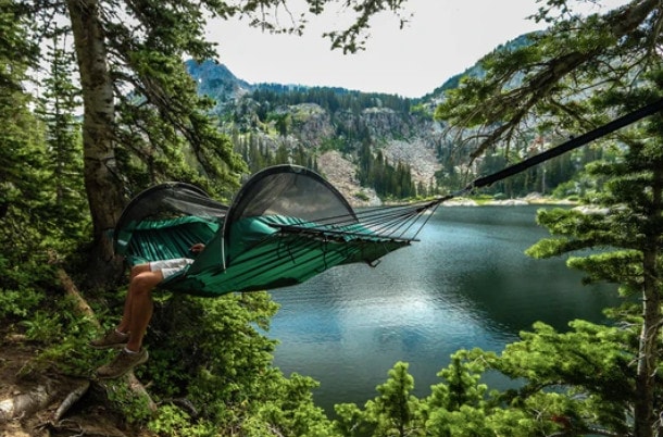 Person sitting on a hammock tent hanging between trees with lake behind