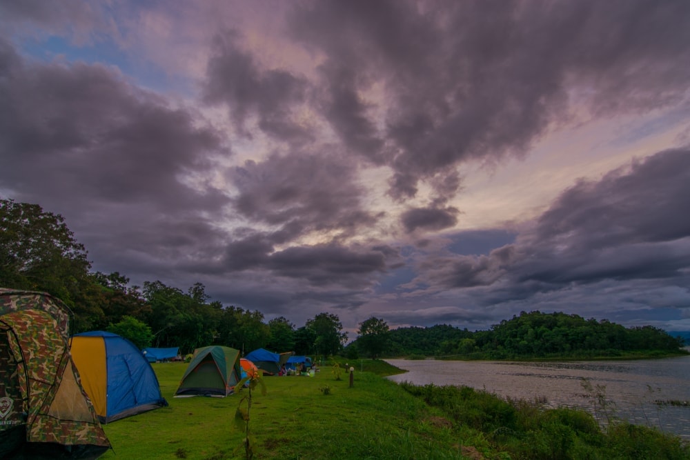 Camping tents lined up beside a river with dark clouds