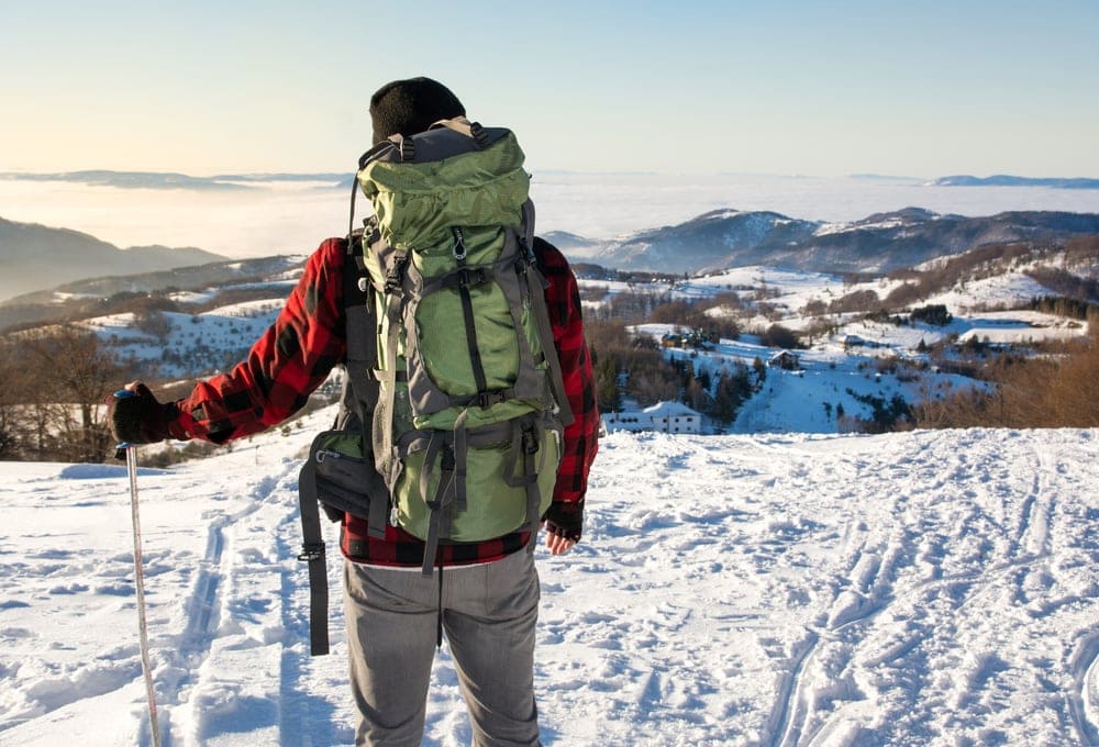Hiker holding a trekking hole and wearing a hiking backpack on a winter morning