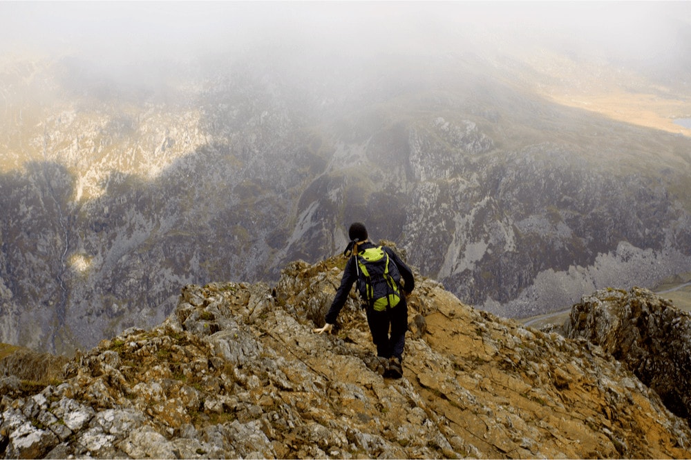 Man hiking and scrambling on top of mountain ridge 