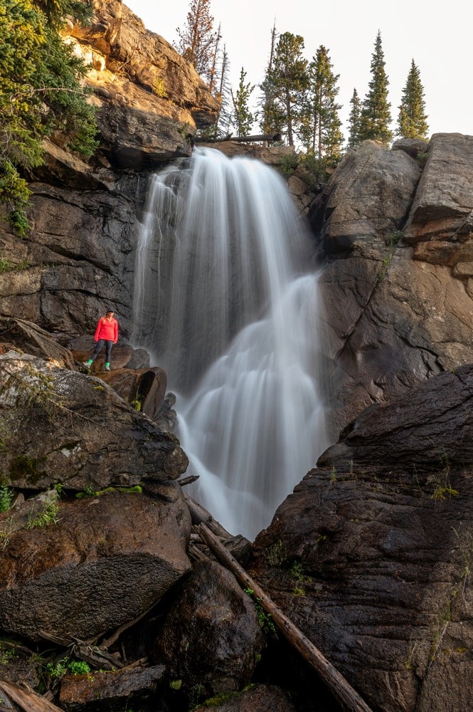 photo of a woman wearing red shirt standing on a big rock near Ouzel falls