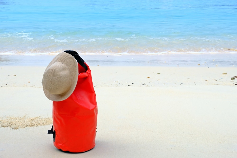 Backpack on white beach sand with hat on it
