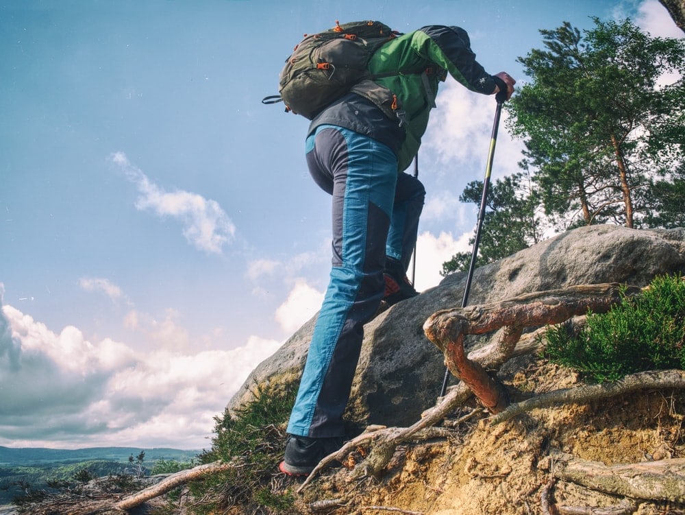 Man climbing up on a rock using trekking poles