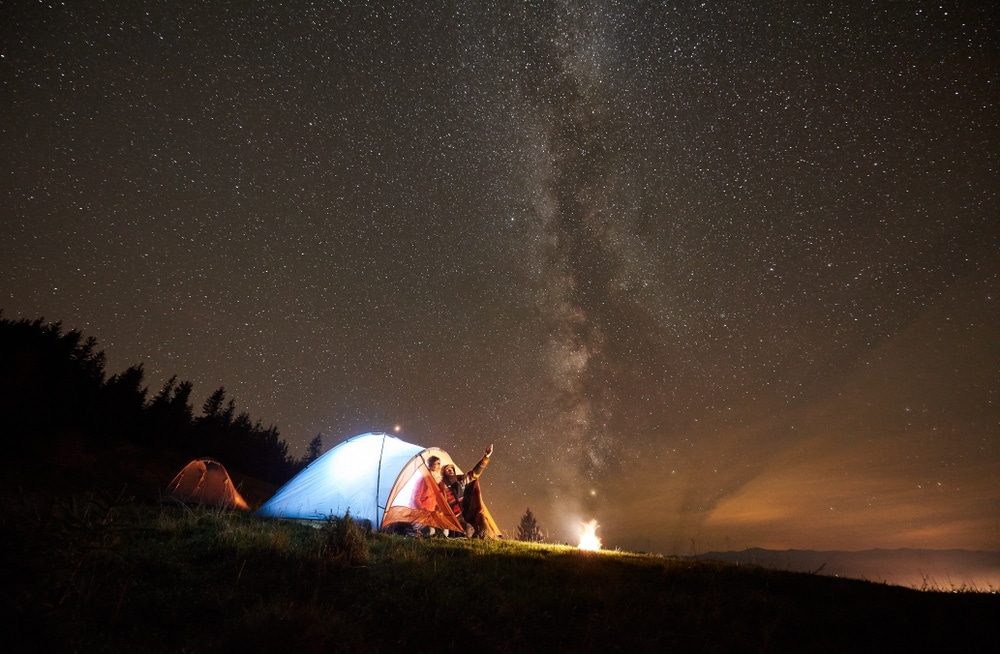 couple camping under the night sky with millkyway near a national forest