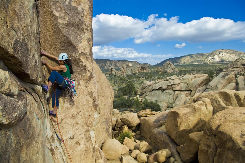 popular things to do in Joshua tree, a female is rock climbing on a steep cliff in Joshua Tree National Park, California.