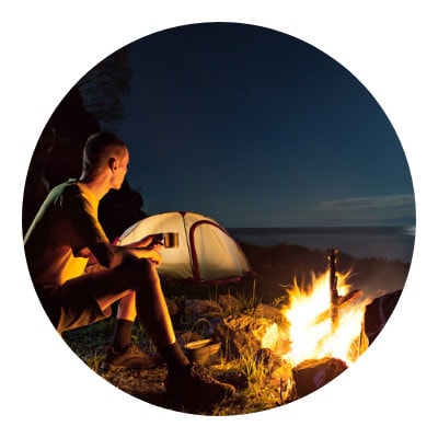 Man sipping his coffee in front of his campfire and tent