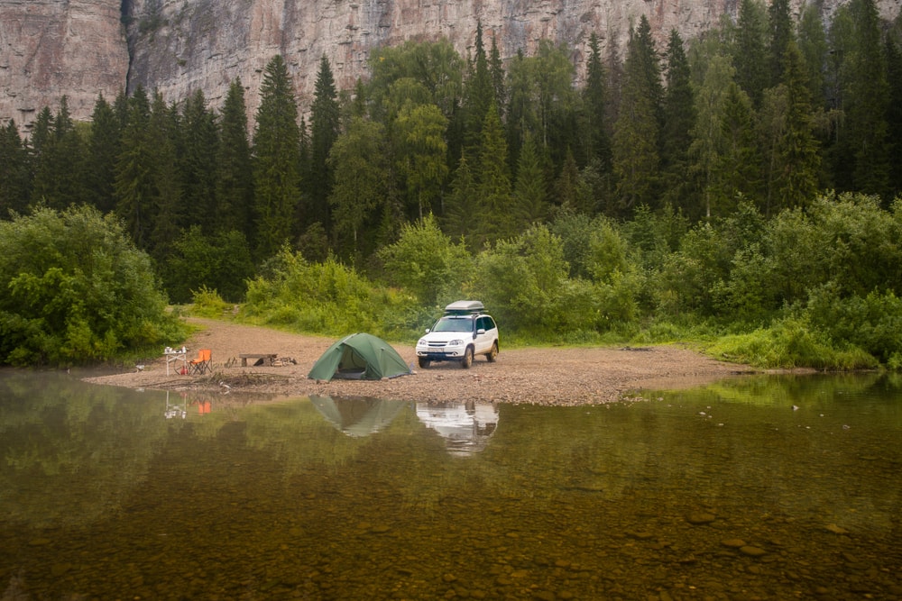 a car and a tent on a campground in the forest near a lake