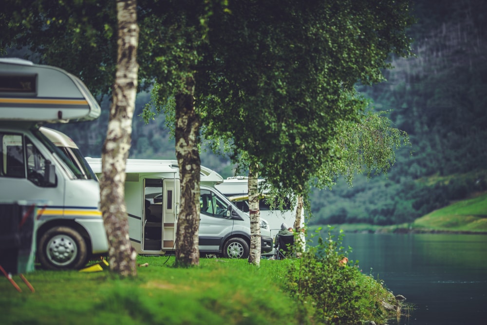 a lane of RV camper parked on a campsite near a lake