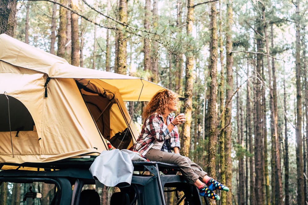 car camping is the most popular camping styles. a woman enjoying a drink on a tent on her car