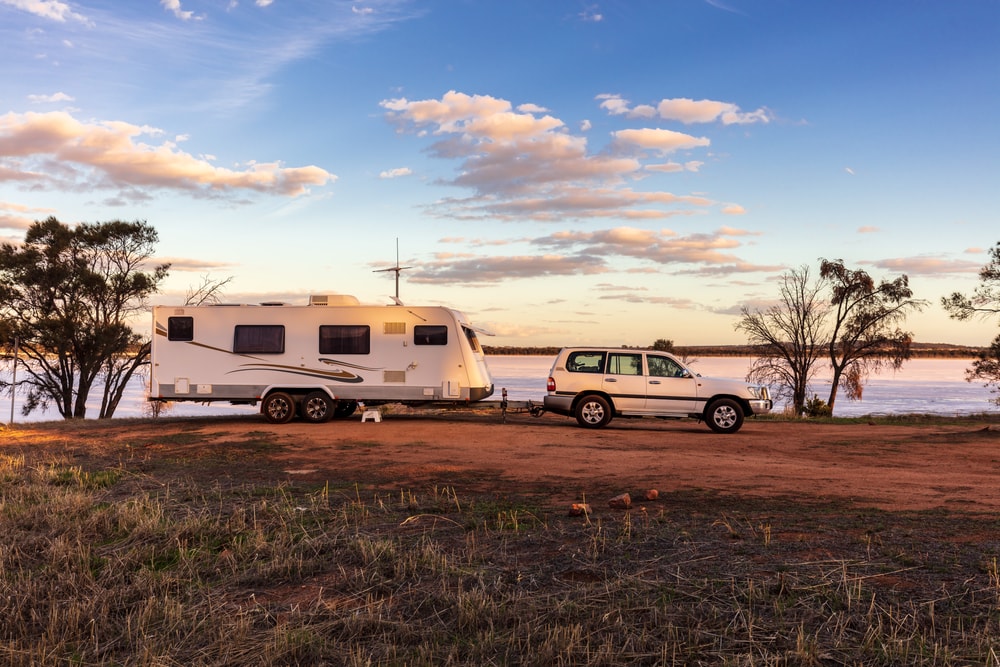 A 4wd car with a RV camp trailer attached parked on a campground near a lake