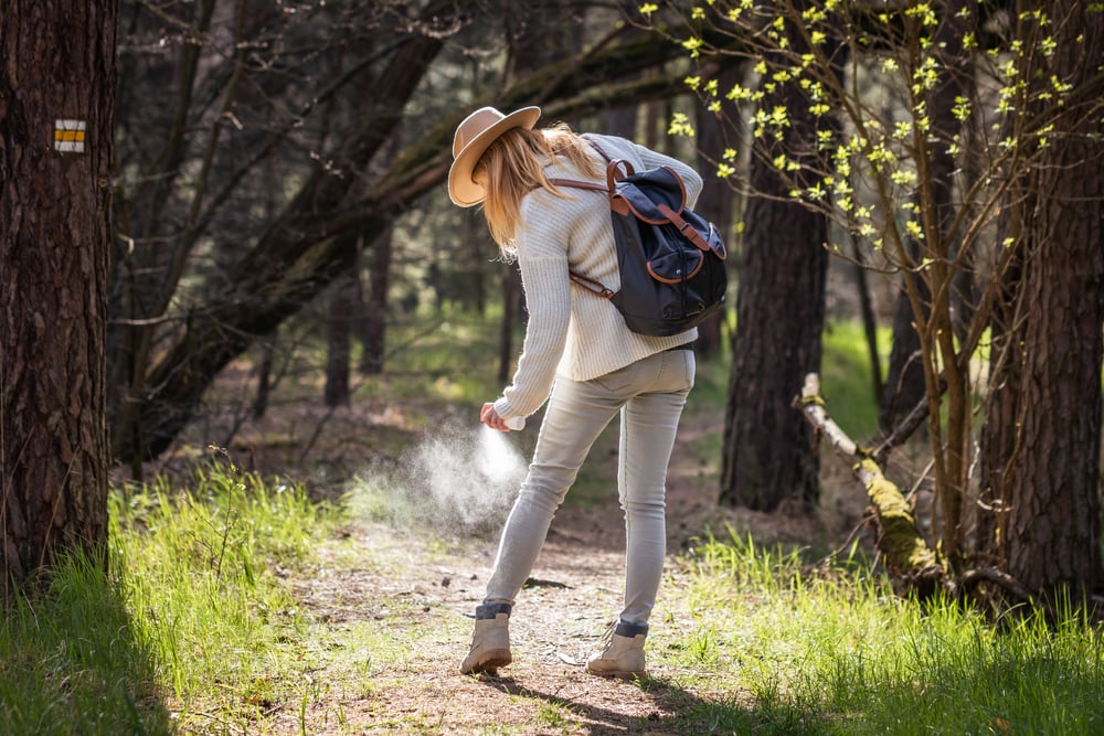 a female in the middle of the forest spraying a bug spray 