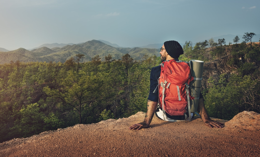 a man sitting alone on a cliff with camping backpack