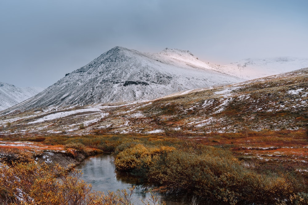 Autumn tundra and cold river on the misty snow-capped mountains, Arctic, Kola Peninsula.