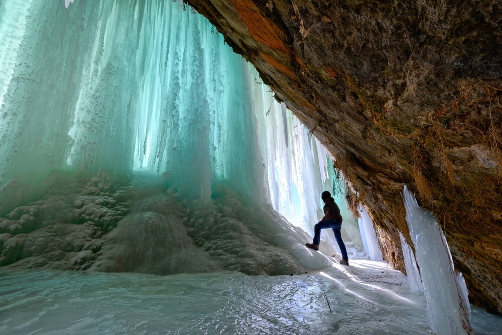 man climbing the ice columns forming across a cave opening on Grand Island, Lake Superior near Munsing, Michigan.