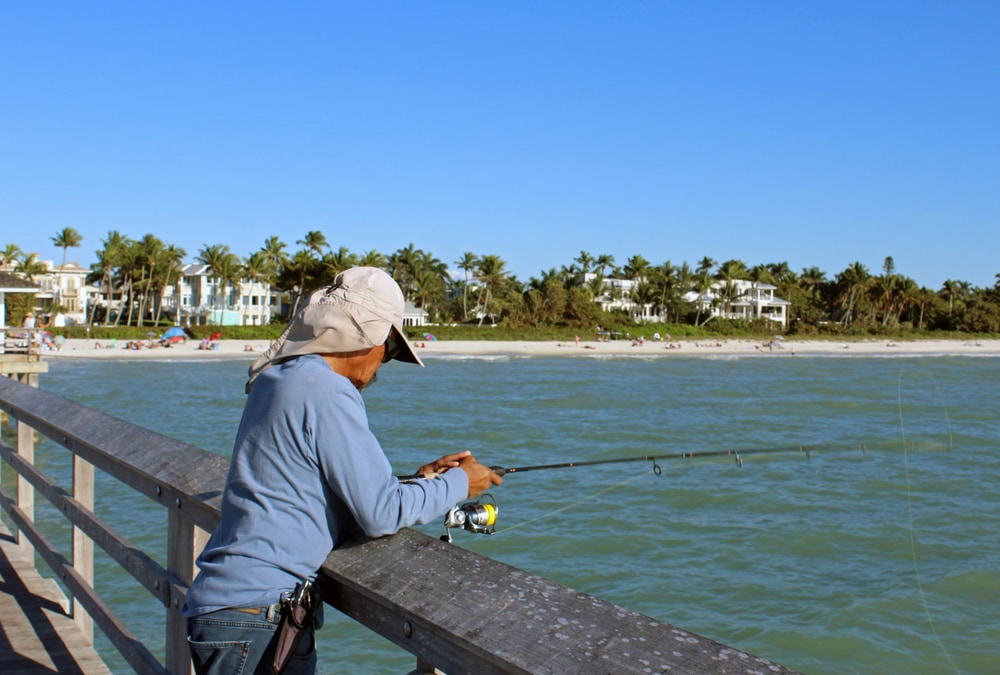 Fisherman holding fishing rod over railing on Naples Pier in Florida.