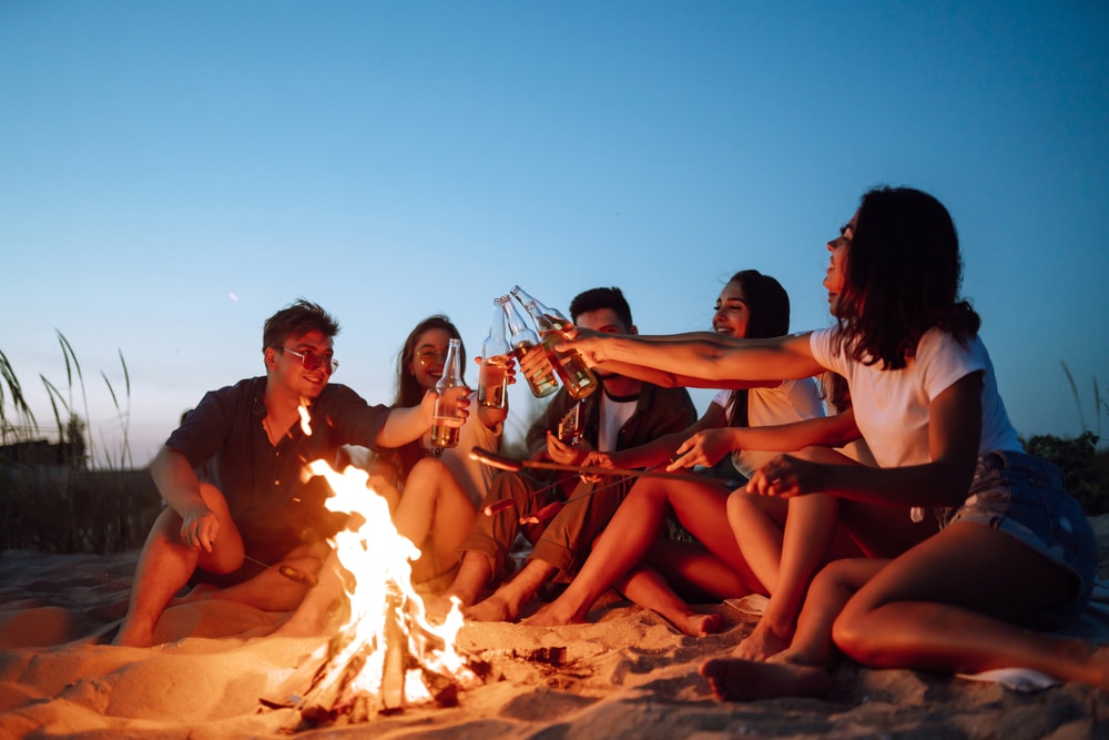 a ground of friends having fun and drinking at a campfire by the beach