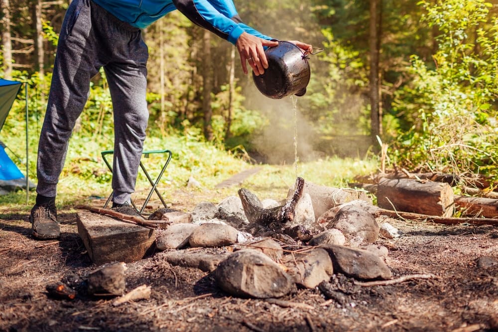 Man putting out a campfire with water from cauldron in summer forest