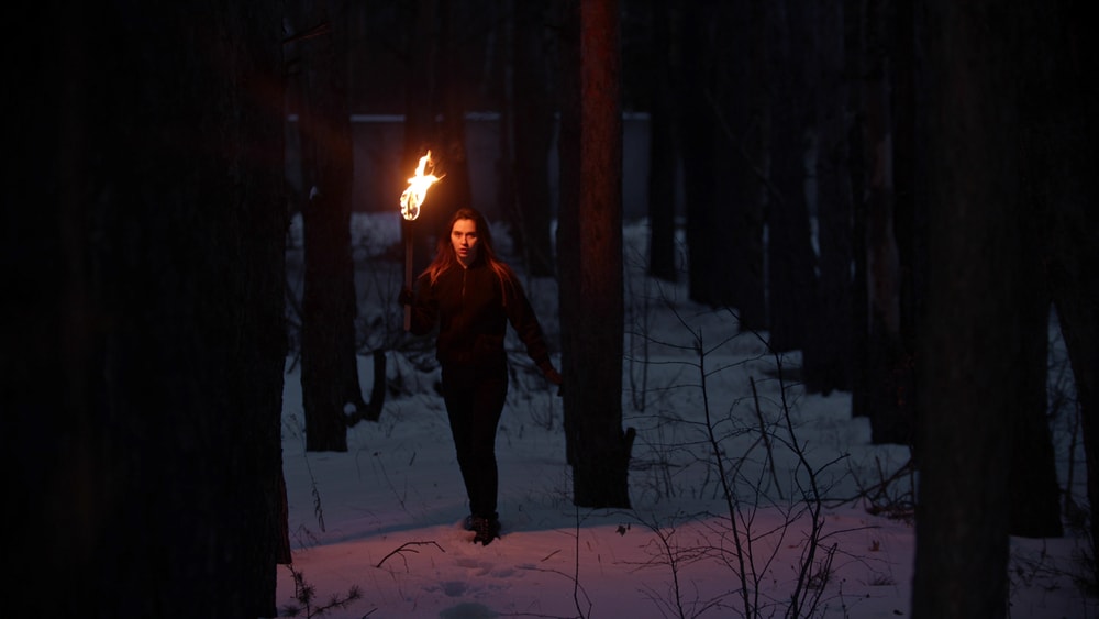 a woman holding a torch to light her way in the middle of a snowy forest