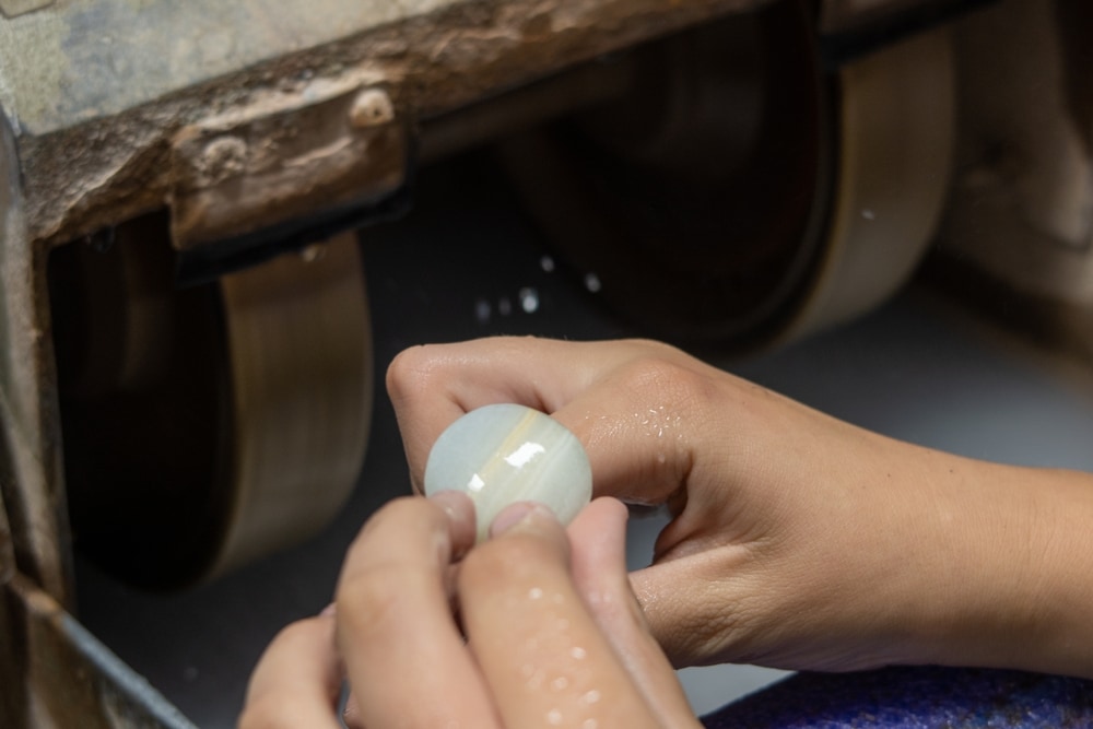 a jeweler grinding and forming a gemstone using a rock grinder in a lapidary shop