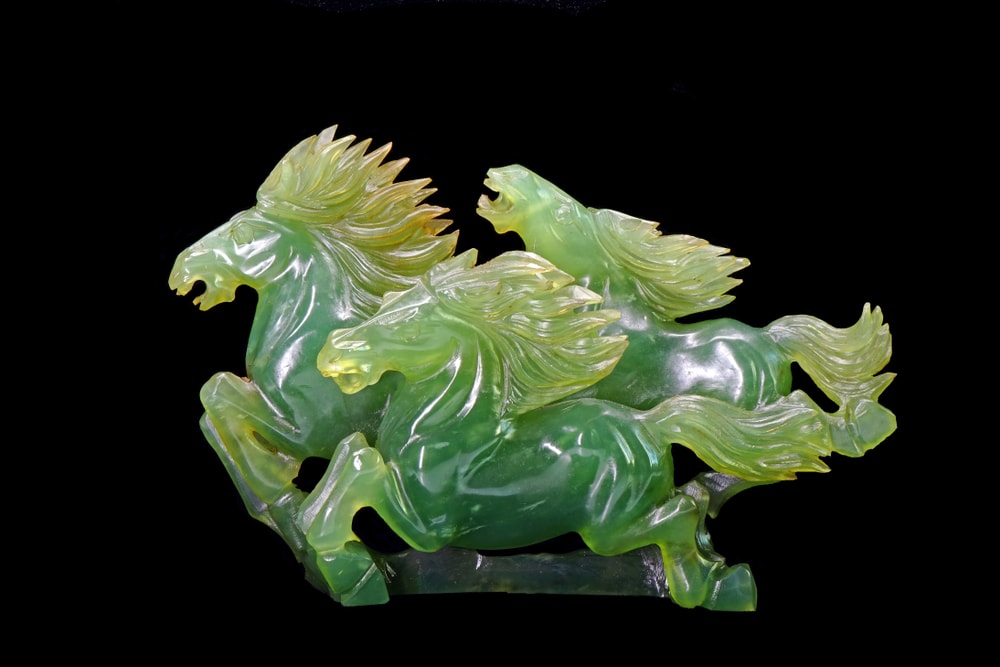 a jade stone sculpted to 3 horses running on a black background