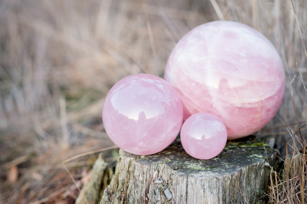 3 rose quartz crystal balls in different sizes laying on a tree in the forest