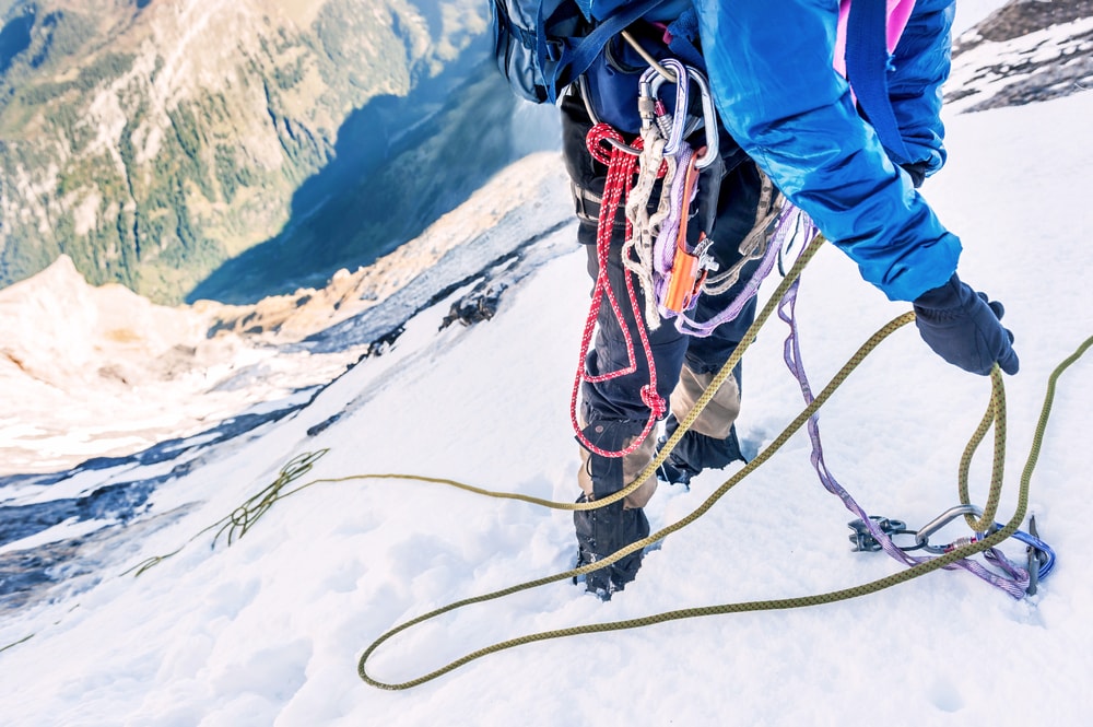 a climber with climbing gears reaching the top of a snowy mountains 