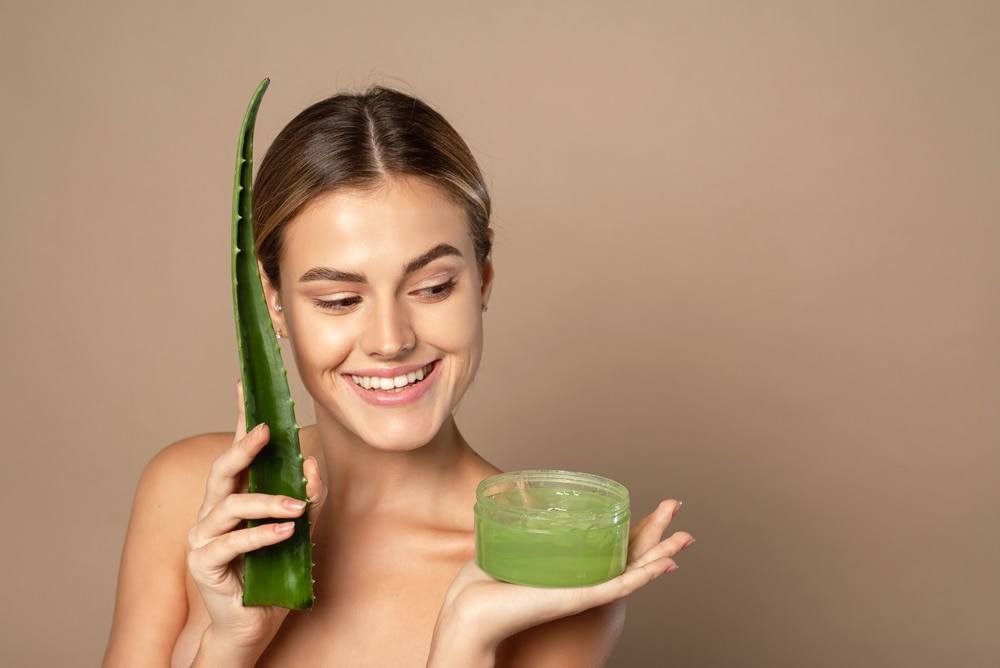 a woman holding an aloe vera plant and aloe vera gel in a container 