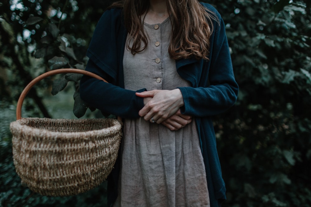 Woman in cardigan holding a basket in the forest