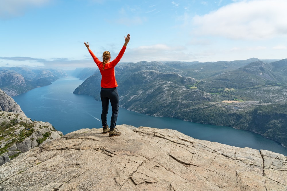 Woman raising its hands on top of a mountain