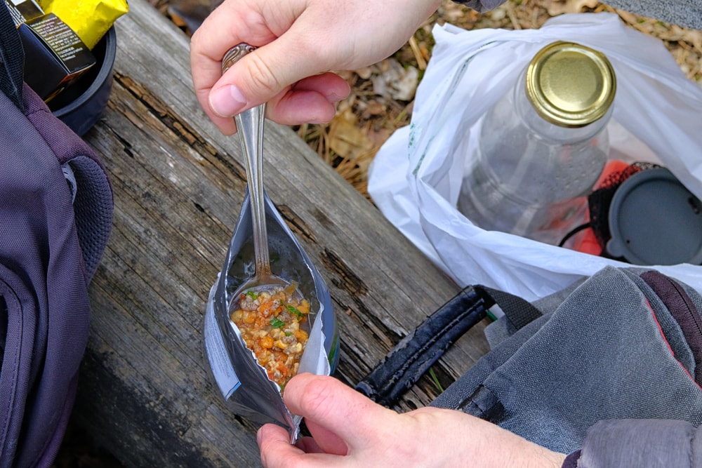 a hiker opening a freeze dried food  in a pouch