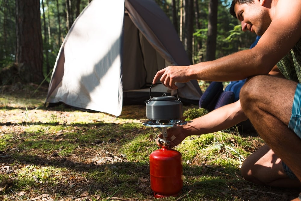 a camper cooking outdoors on a propane camping stove