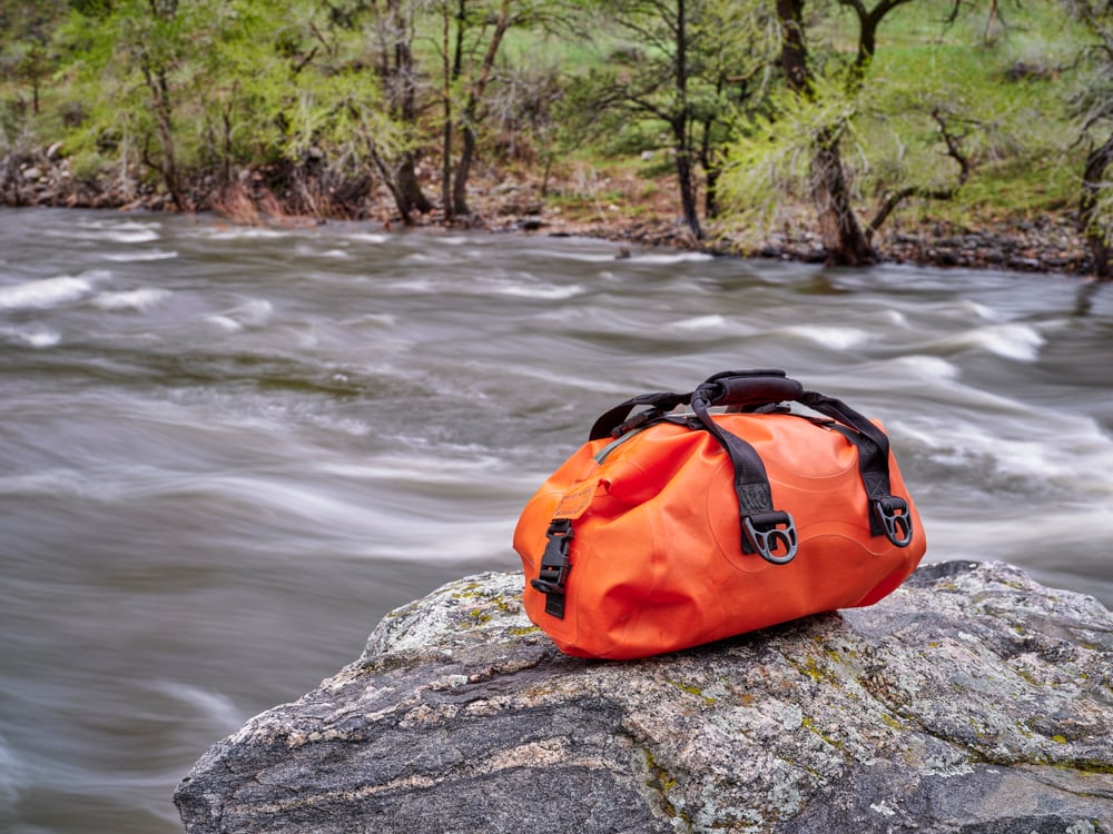 a duffle bag on top of a boulder by the river