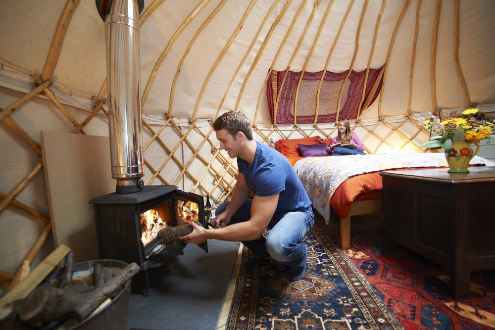 a man putting kindling on a wooden furnace in a yurt