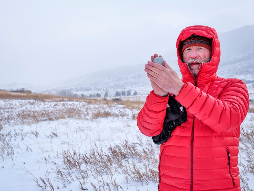 image of a man wearing a jacket and holding a hand warmer in a snowy mountain