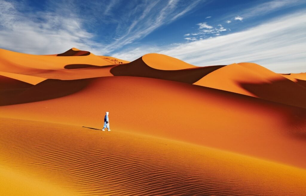 a man walking on the sand dunes in Sahara desert