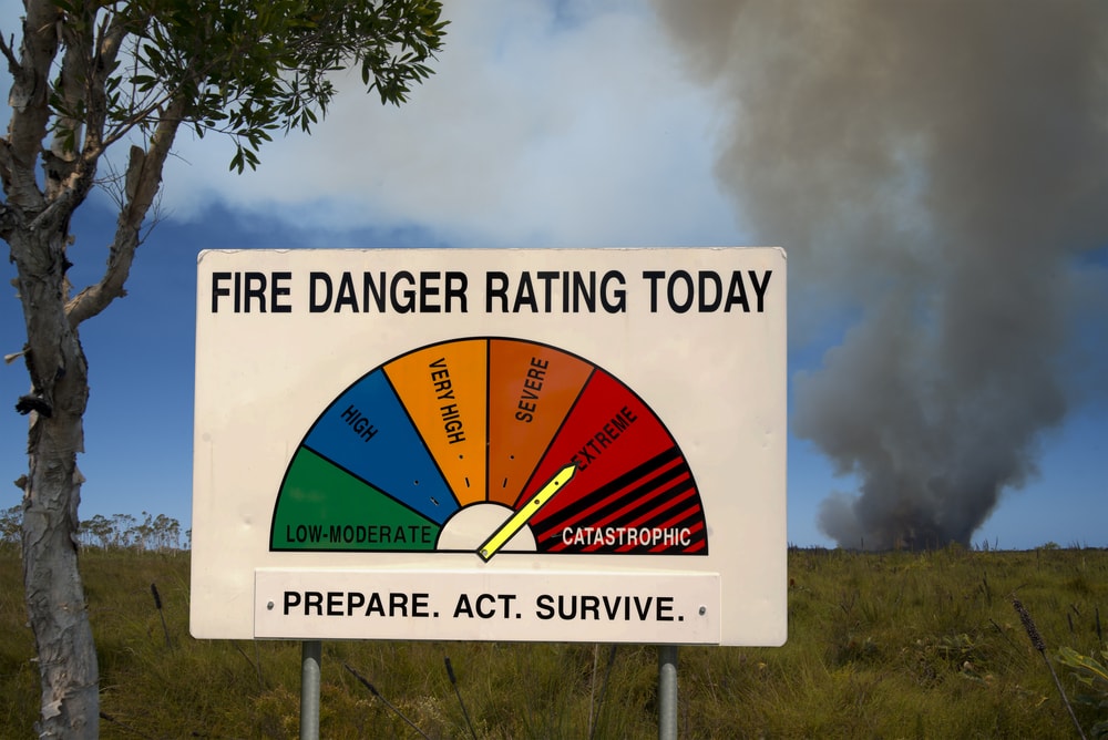 fire danger rating display board with a bushfire smoking in background.
