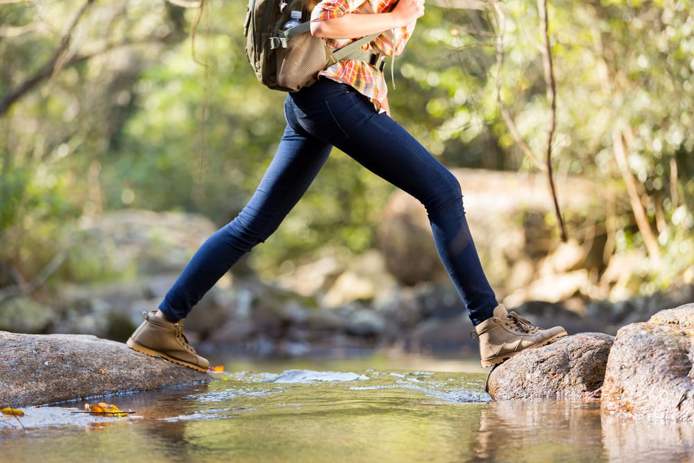 A woman crossing a river while hiking in jeans 