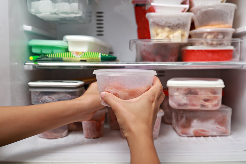 Woman putting a  container with frozen meat  in the refrigerator